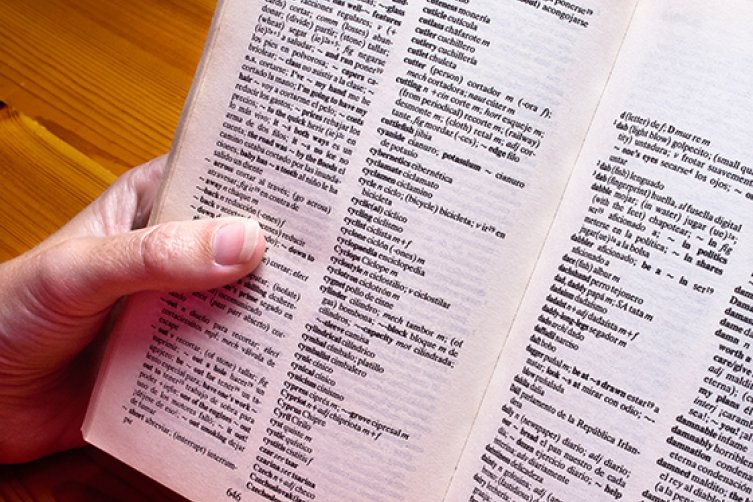 Wörterbücher auf einem Schreibtisch, die von einer Hand gehalten werden